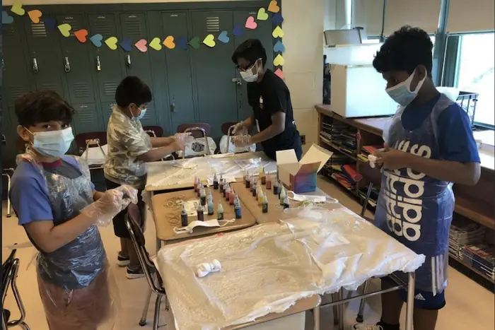 A group of young students wearing masks work on a school project.